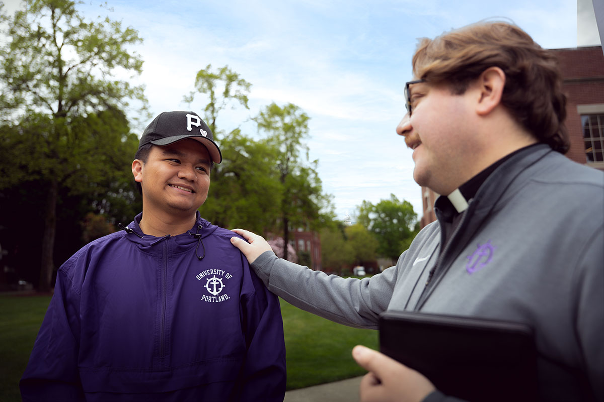 father nick places his hand on the shoulder of a smiling student