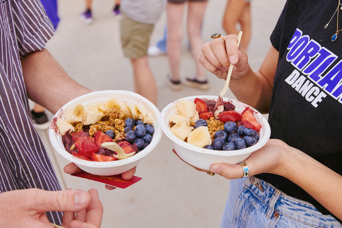 A close-up view of two UP students at a campus food truck event holding acai smoothie bowls topped with fruit and granola. 
