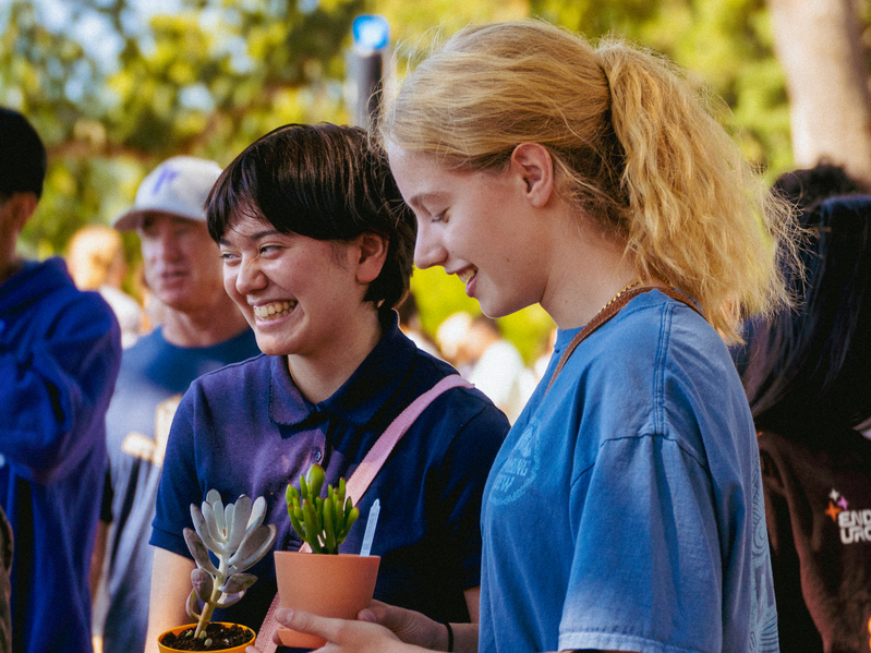 Two University of Portland students smile and hold potted plants during the Wellness Fair. 