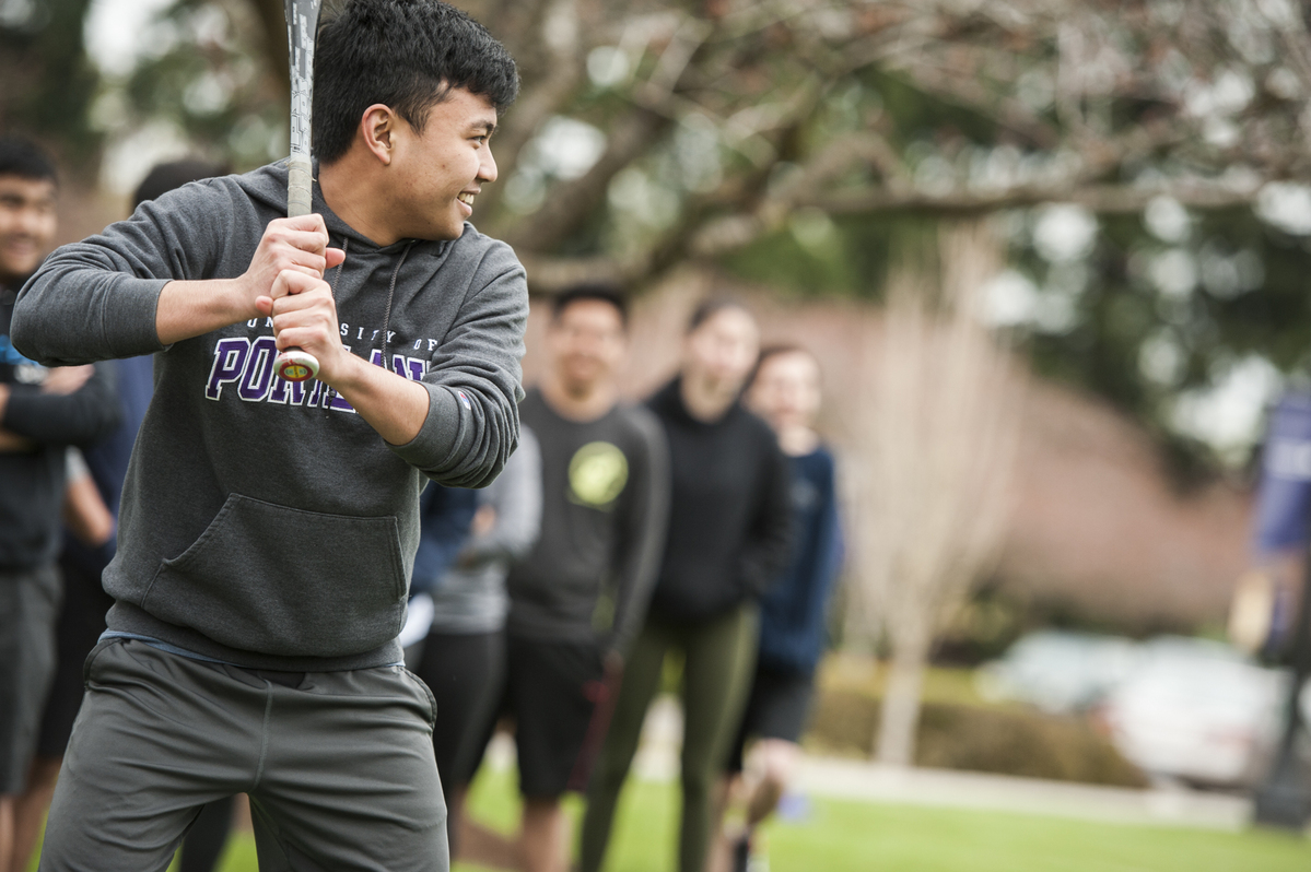 A smiling UP student stands with a baseball bat ready to swing during an intramural softball game