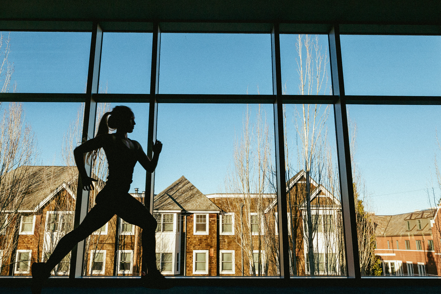 A student's silhouette from inside the Beauchamp Recreation Center as they run on an indoor track in front of a large window.