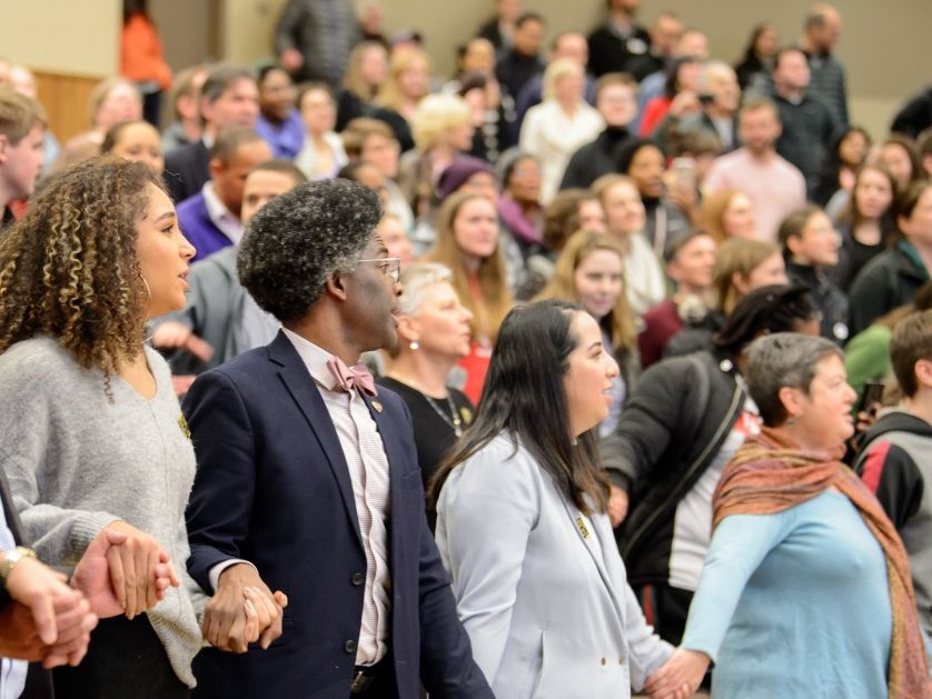 A wide angle image of UP faculty and staff holding hands and singing at an MLK Day celebration.